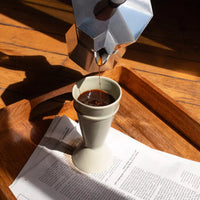 cafetière italienne utilisée pour servir le café dans un mazagran vert qui est sur un plateau en bois