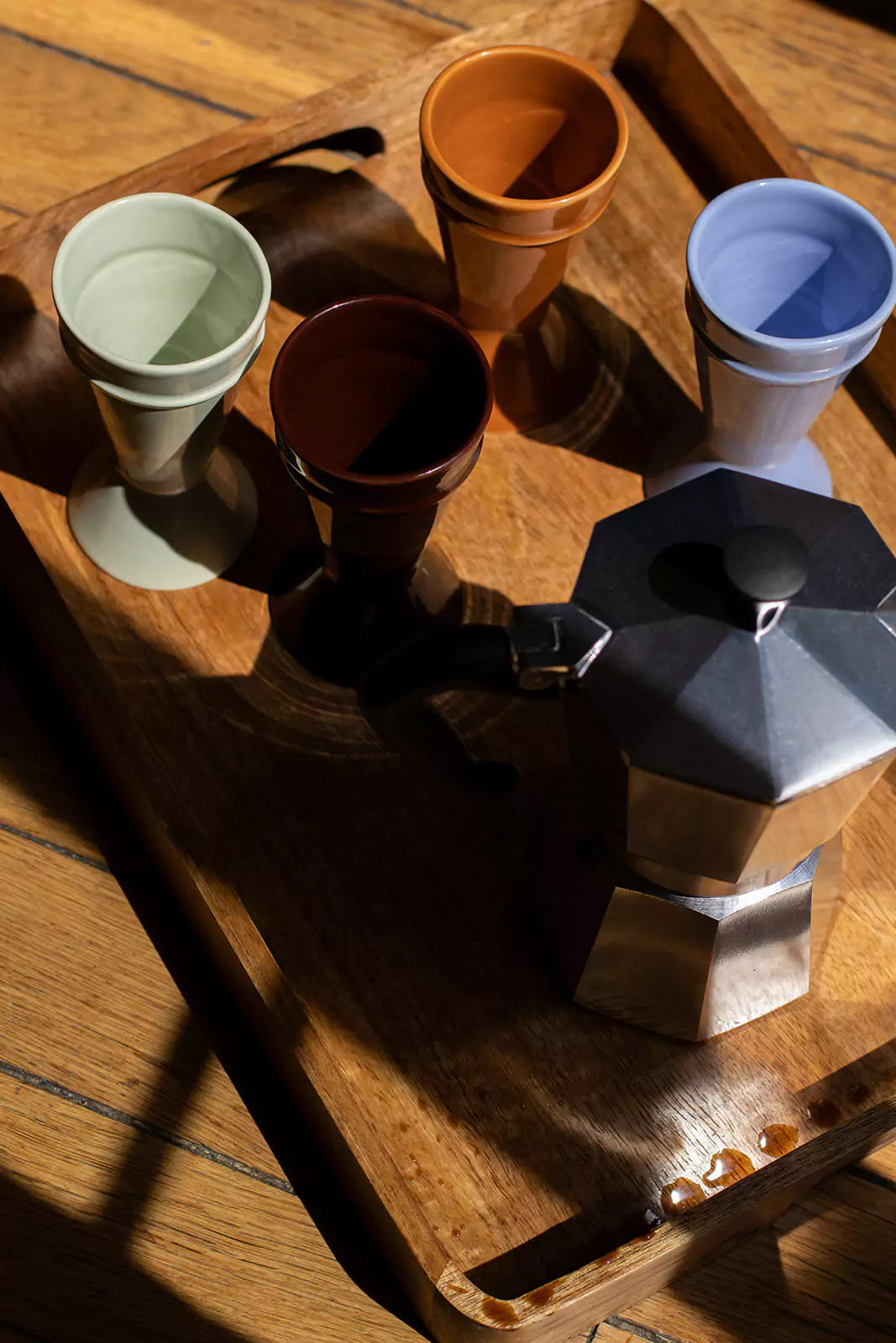 Collection de tasses mazagran en grès colorées disposées sur un plateau en bois avec cafetière italienne – Atelier Maison Quatre.